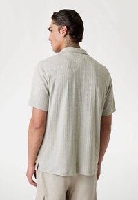 Short-sleeved shirt in light gray with a textured geometric pattern, featuring a collared neckline and side slits for added movement.