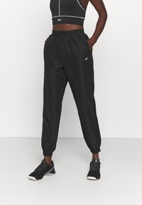 Černé, lehké zúžené tepláky s elastickými lemy, bočními kapsami a nastavitelným stahovacím pasem. Hladká textura, minimální detaily.