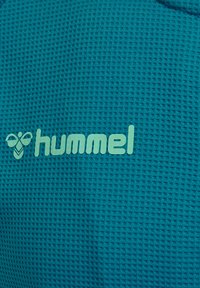 Turkos texturiserad tyg med ett honungskombmönster och en ljusblå "hummel"-logotyp som står ut.