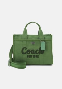 Grön canvasväska med två korta handtag, en justerbar axelrem och en stor broderad logotyp "Coach New York". Silverfärgade detaljer.