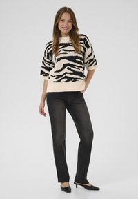Knitted oversized sweater in cream with black zebra stripes, paired with dark jeans. The sweater features short sleeves and a rounded neckline.