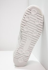 Weiße Sportschuhsohle aus strukturiertem Gummi mit runden und gerippten Mustern. Verfügt über ein eingeprägtes Logo und ein glattes Kantendesign.