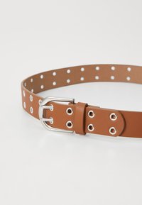 Cinturón de imitación cuero marrón con hebilla de metal plateado, que presenta una fila de ojales redondos espaciados de manera uniforme a lo largo de su longitud para el ajuste del tamaño.