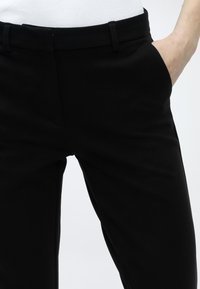 Μαύροι ραμμένοι παντελόνες με ομαλή υφή, κανονική μέση, πλαϊνές τσέπες και στενή εφαρμογή. Κατασκευασμένοι από μαλακό υλικό.