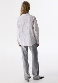Camisa blanca de manga larga con textura y cuello, combinada con pantalones gris de pierna ancha que presentan lentejuelas dispersas y un ajuste casual.