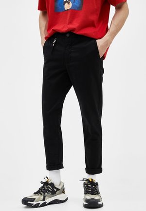 Černé kalhoty s zužujícím se střihem, ohrnuté u kotníků. Spárované s vícero barevnými teniskami s texturovanou podrážkou a tkaničkami.