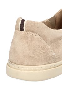 Beżowy zamszowy sneaker o zaokrąglonym kształcie, z kontrastującym brązowym akcentem na pięcie oraz teksturowaną gumową podeszwą z detalami szwów.