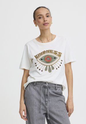Femme portant un T-shirt blanc avec un dessin stylisé d'un œil et le mot "BONTÉ", associé à un jean gris taille haute.