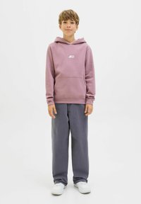 Pinky hoodie med framficka och vitt logotyp, kombinerad med grå vida byxor och vita sneakers, placerad på en ren vit bakgrund.