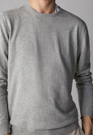 Homme portant un pull uni gris clair à manches longues et col rond, vu du cou jusqu'aux hanches sur un fond neutre.