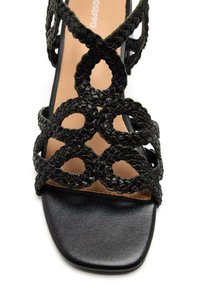 Sandalini neri con tacco alto e cinturini intrecciati, con tagli circolari, punta quadrata e suola nera liscia con soletta beige.