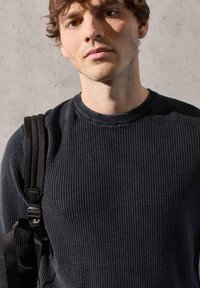 Pull noir côtelé avec un col rond, tissu texturé et coupe slim. Comprend une sangle réglable d'un sac à bandoulière.