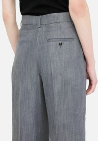 Gray tailored trousers with a subtle texture, featuring a back pocket and button detail. Straight fit with a mid-rise waistline.