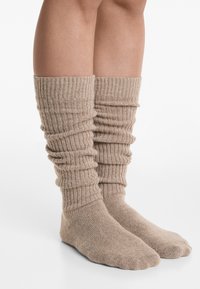Beige ribbede knæ-høje sokker med sammensnøring øverst, lavet af et blødt materiale og med en sømløs tå-design.