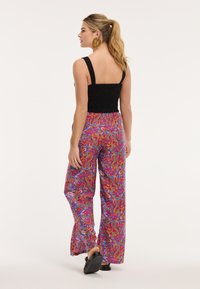 Fekete fűzött crop top vastag pántokkal, élénk mintájú, lazán illeszkedő nadrággal, amely rózsaszín, lila és narancssárga árnyalatokban pompázik.