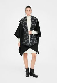 Poncho nero con colletto grigio a motivo, realizzato in tessuto misto lana. Presenta un design ampio ed è abbinato a stivali alla caviglia.