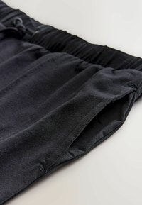 Schwarze Jogginghosen aus weichem Stoff, mit einem elastischen Bund und seitlichen Taschen. Das Material wirkt glatt mit einem leichten Glanz.