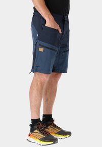 Pantaloni corti blu navy con molteplici tasche con zip, texture contrastanti e logo STX. Abbinati a scarpe da ginnastica nere e arancioni.