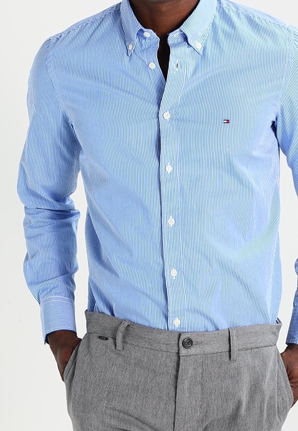 Camisa de botón a rayas azul claro con cuello y botones blancos. Combinada con pantalones grises, que presentan un diseño sencillo y una tela texturizada.