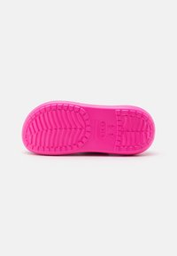 Semelle de chaussure rose vif avec motif de la bande de roulement et le nom de la marque "Crocs" embossé près du centre, sur un fond clair uni.