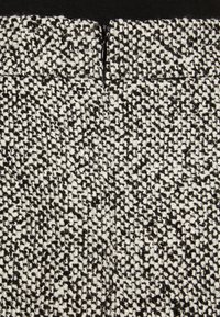 Detailní záběr na černobroušenou látku s texturou a malým vertikálním zipem uprostřed blízko horního okraje.