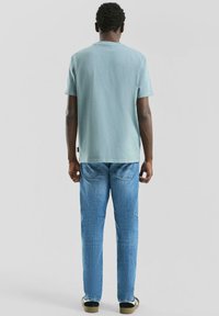 T-shirt en coton vert menthe à manches courtes, assorti à un jean en denim bleu clair. La tenue comprend des baskets noires et blanches.