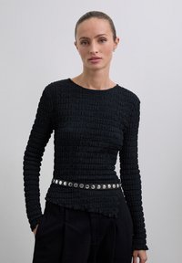 Zwarte, gestructureerde top met lange mouwen en een geplooid ontwerp, aangevuld met een zilveren studs riem op de taille.