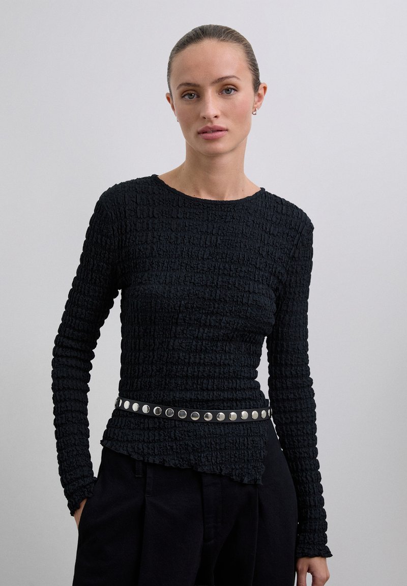 Zwarte, gestructureerde top met lange mouwen en een geplooid ontwerp, aangevuld met een zilveren studs riem op de taille.