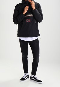 Černá mikina s kapucí, která má přední kapsu na zip, značenou nášivku a detail norské vlajky. Nosí se s černými džíny a botami Vans.