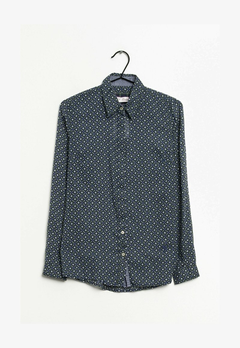 Chemise bleu foncé à manches longues avec boutons et pois blancs et bleu clair, accrochée sur un cintre noir sur fond blanc.