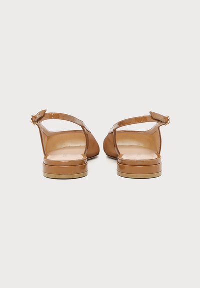 Paire de ballerines slingback en cuir verni beige avec petits talons empilés, photographiées de dos sur fond blanc uni.