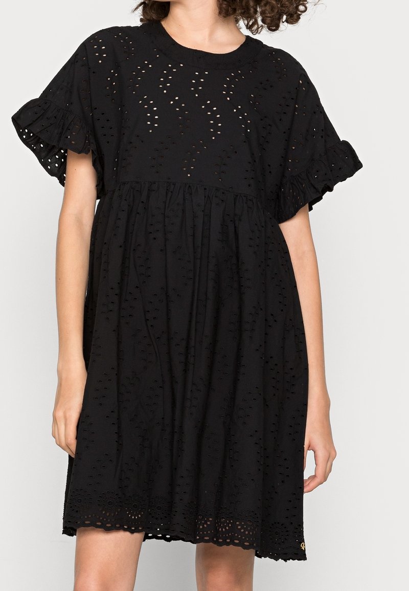 Vestido negro con mangas cortas acampanadas, que presenta un diseño de ojetes y un corsé acampanado. Dobladillo texturizado con recortes florales. Tejido ligero.