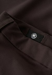 Ceinture élastique ajustable avec bouton sur un tissu brun foncé, montrant le détail de la couture et la texture du tissu.