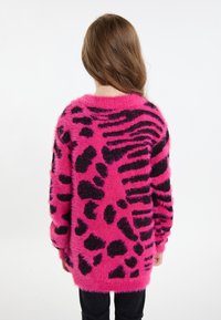 Purus rožinis megztinis su juodu gyvūnų raštu, turintis ilgus rankovėmis ir laisvą sijoną, besitęsiantis iki klubų, tekstūruota paviršius.