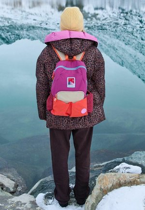 Kurtka puffer w panterkę z różowymi i fioletowymi akcentami, brązowe spodnie oraz wielokolorowy plecak z różowymi, fioletowymi i pomarańczowymi detalami.