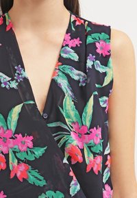 Blusa floral en azul marino oscuro con vibrantes patrones tropicales en rosa y verde, que presenta un escote en V profundo y una tela suave y transparente.