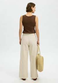 Brun utanärmad topp i kombination med vida, beige randiga byxor. Modellen bär en vävd beige väska, vilket framhäver en avslappnad silhuett.