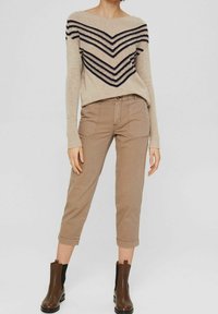 Ljusbeige tröja med marinblå chevront mönster, texturerad väv; matchad med ljusbruna cropped chinos och bruna ankelstövlar.