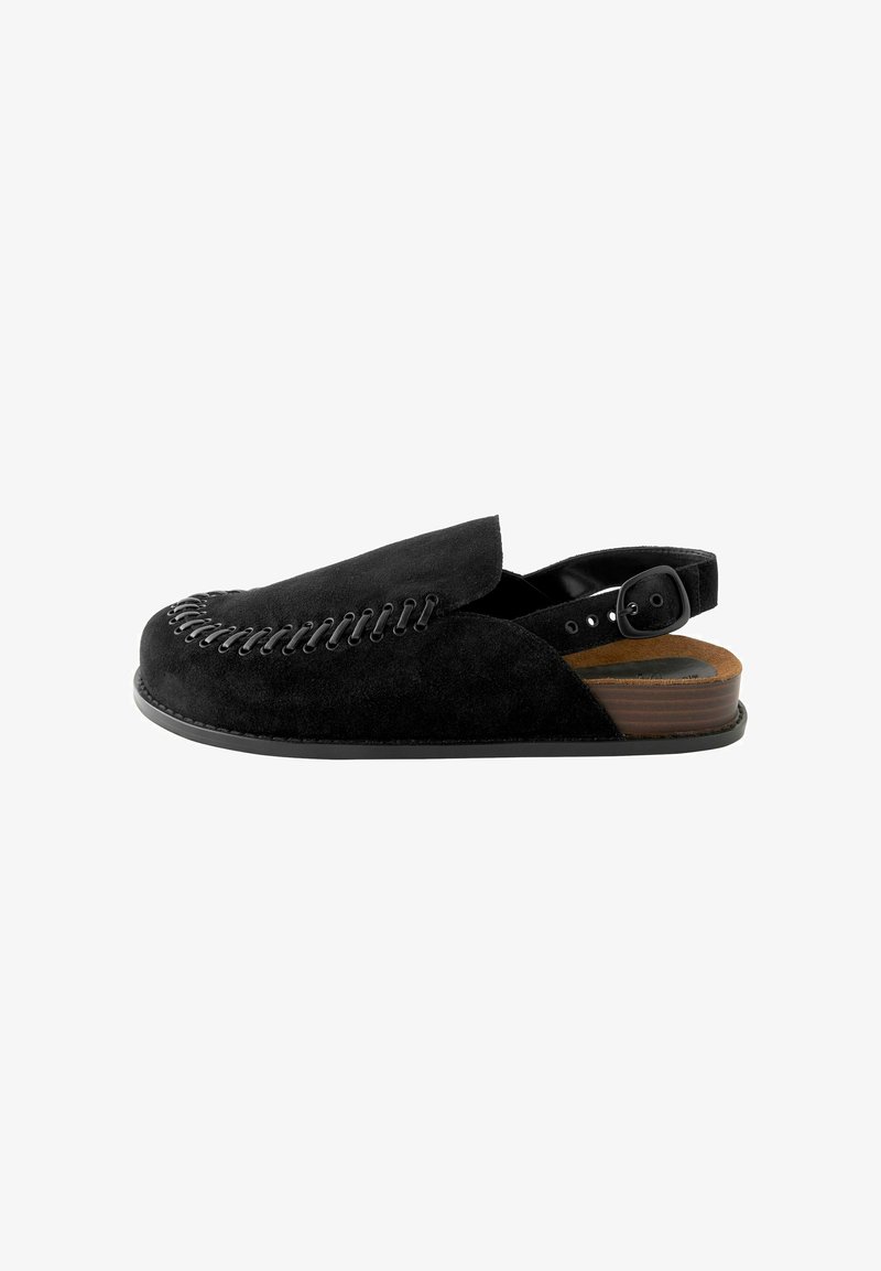 Black suede slip-on shoe with a rounded toe, detailed stitching along the front, and an adjustable buckle strap at the heel. Brown wooden sole.