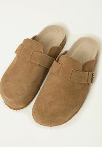 Brown suede clogs with a strap and buckle detail. Rounded toe and soft, textured material, featuring a cushioned insole and flat sole.
