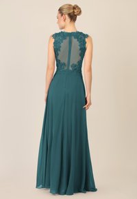 Vestido de noche en color azul verdoso con un respaldo de encaje transparente, bordados florales en los hombros y una falda fluida. Cierre con cremallera en la parte posterior.