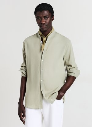 Chemise vert clair à manches longues avec col mandarin, texture légère et fermeture à boutons ; accompagnée d'une écharpe jaune à motifs.