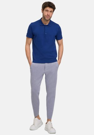 Granatowa koszulka polo z trzema guzikami, w zestawieniu z jasnoszarymi spodniami o tapered fit z przeszyciami i białymi sneakersami.