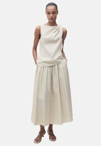 Beige top bez rukávů s asymetrickým detailem na rameni, spárovaný s odpovídajícími plisovanými midi sukni; hladká textura a minimalistický design.