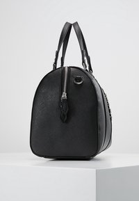 Svart handväska med rundad form, texturerat material, dubbla handtag och en framträdande silverdragkedja. Har en elegant design och subtila hårdvaruaccenter.