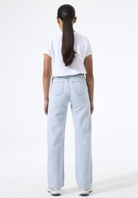 Vaqueros de tiro alto en azul claro con un ajuste relajado y pierna estrechada, combinados con una camiseta blanca de manga corta y zapatillas, vistos desde atrás.