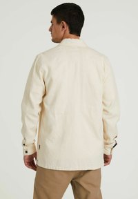 Camicia di cotone color crema con yoke sul retro, polsini abbottonati e dettagli di cucitura visibili. Presenta una vestibilità rilassata e una texture liscia.