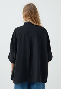 Black oversized shirt with short sleeves, made of soft, lightweight fabric. Features a back yoke and a relaxed fit.
