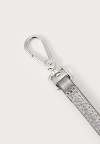 Metallf fjeder snap-hook fastgjort til en sølv læderrem med en tekstureret overflade. Metaldele er skinnende og sølvfarvede.