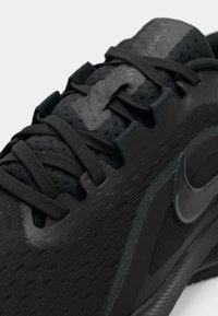 Μαύρο αθλητικό παπούτσι με επάνω μέρος από δίχτυ, επίπεδα κορδόνια και υφασμένη σόλα. Διαθέτει γυαλιστερό μαύρο λογότυπο Nike και ενισχυμένη φτέρνα.